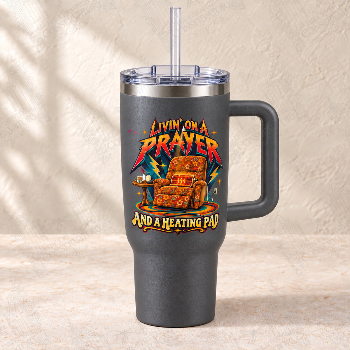 Livin’ on a Prayer and a Heating Pad on charcoal-gray 30-ounce Big Swig with clear reusable straw; faint diagonal Wondergate watermark across the entire image
