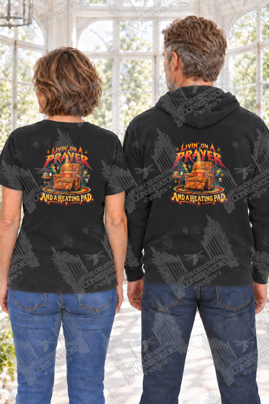 Livin’ on a Prayer and a Heating Pad — back print on approved middle-aged T-shirt and hoodie models; proportional 10-inch-wide artwork; faint diagonal Wondergate watermark across the entire image