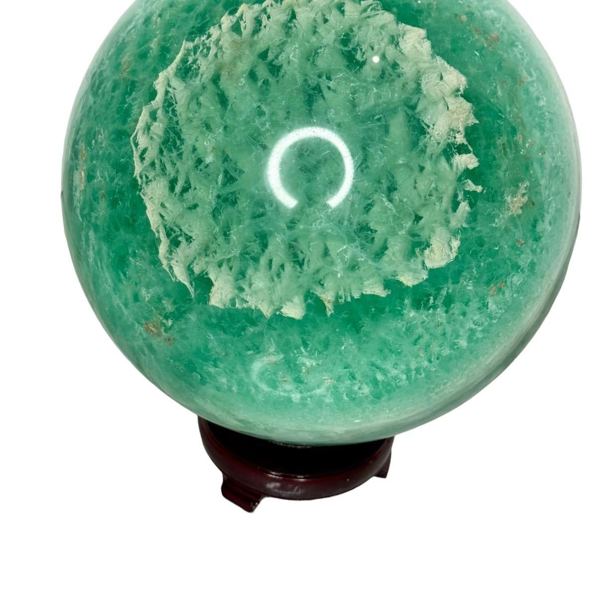 Large green feather fluorite sphere with white feather-like patterns on a dark wooden stand