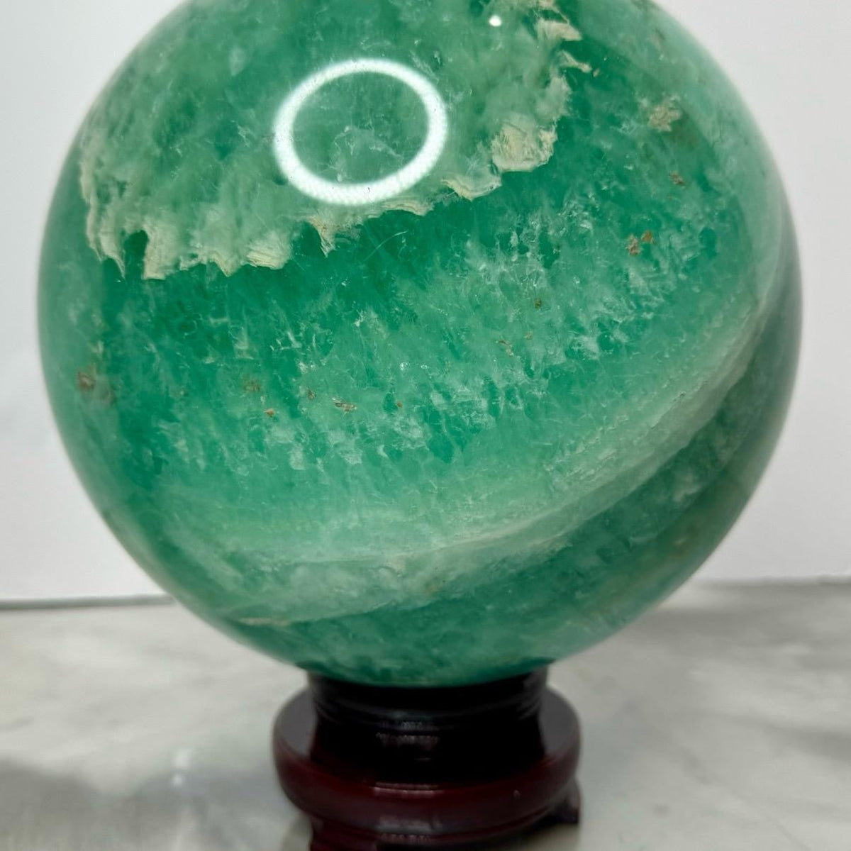 Alternate view of the exact large green feather fluorite sphere showing white feather-like patterns and wooden display stand